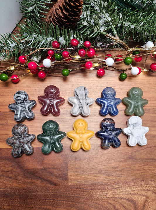 A collection of colorful gingerbread man figurines arranged on a wooden surface, with a pine cone and Christmas decorations visible in the background.