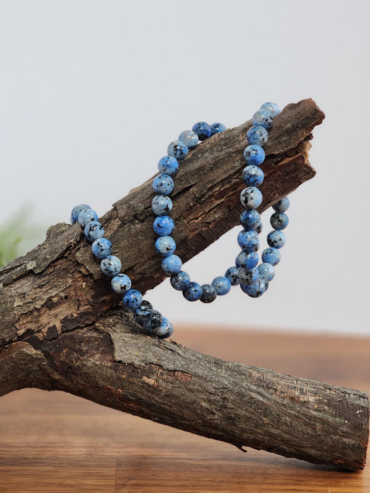 A necklace of blue and black stones is displayed on a wooden surface, with the stones arranged in a loose, natural manner.