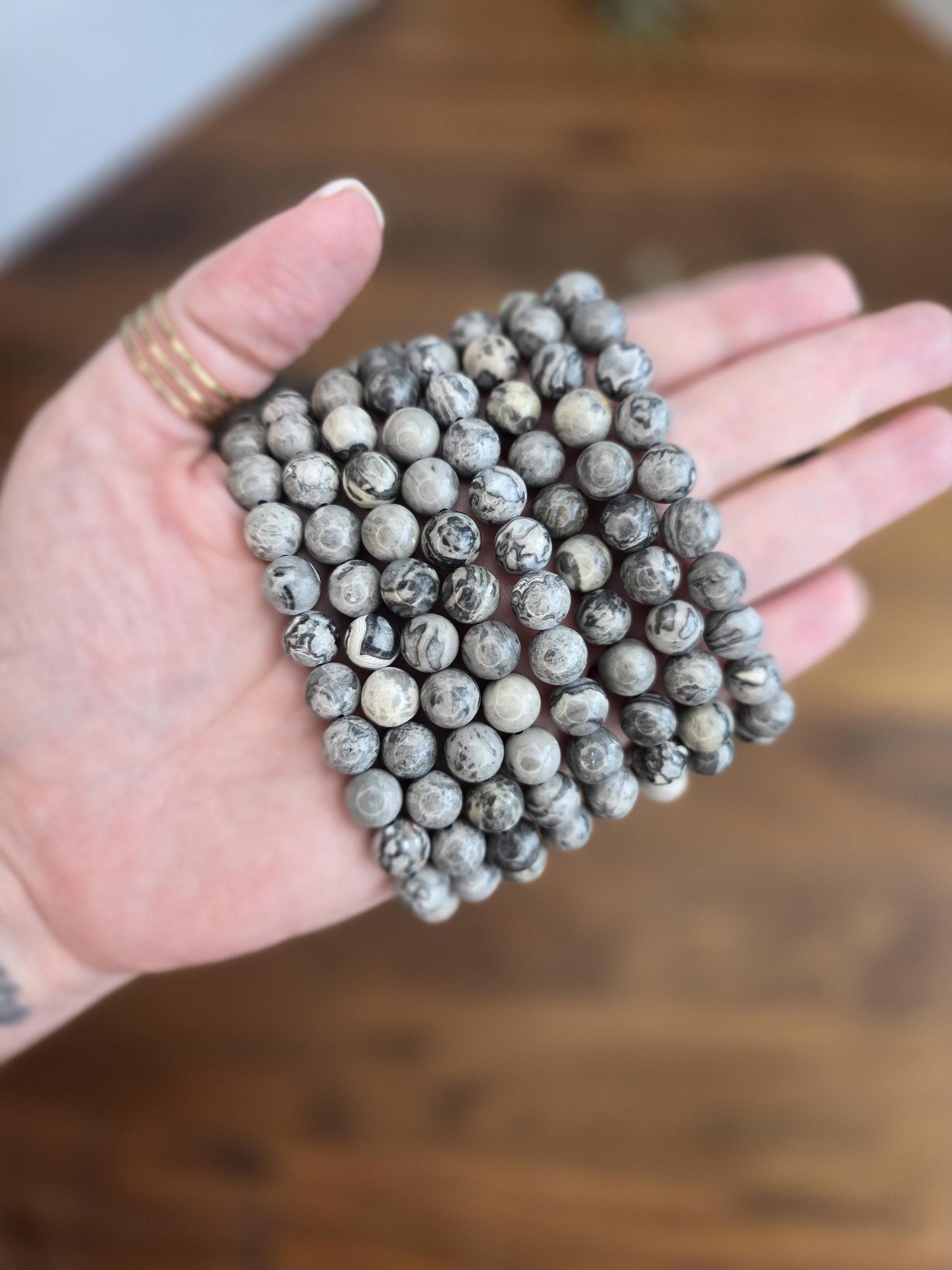 May include: A stack of gray and black gemstone beads, each bead has a unique swirling pattern.