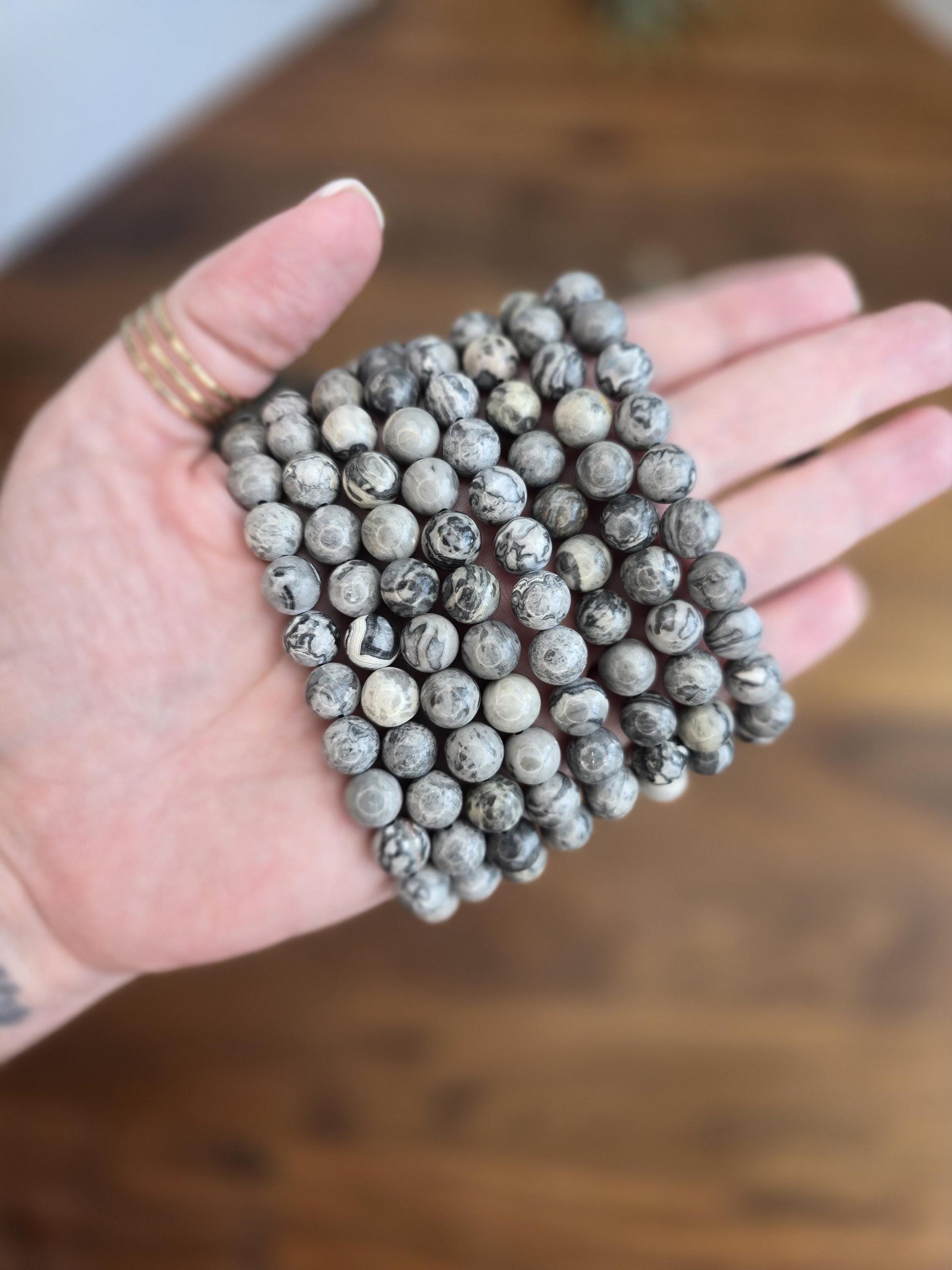 May include: A stack of gray and black gemstone beads, each bead has a unique swirling pattern.