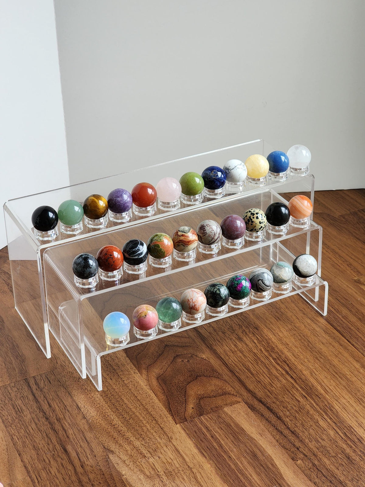 A clear glass display case containing various colorful gemstones, including amethyst, jade, and turquoise, arranged on three shelves.
