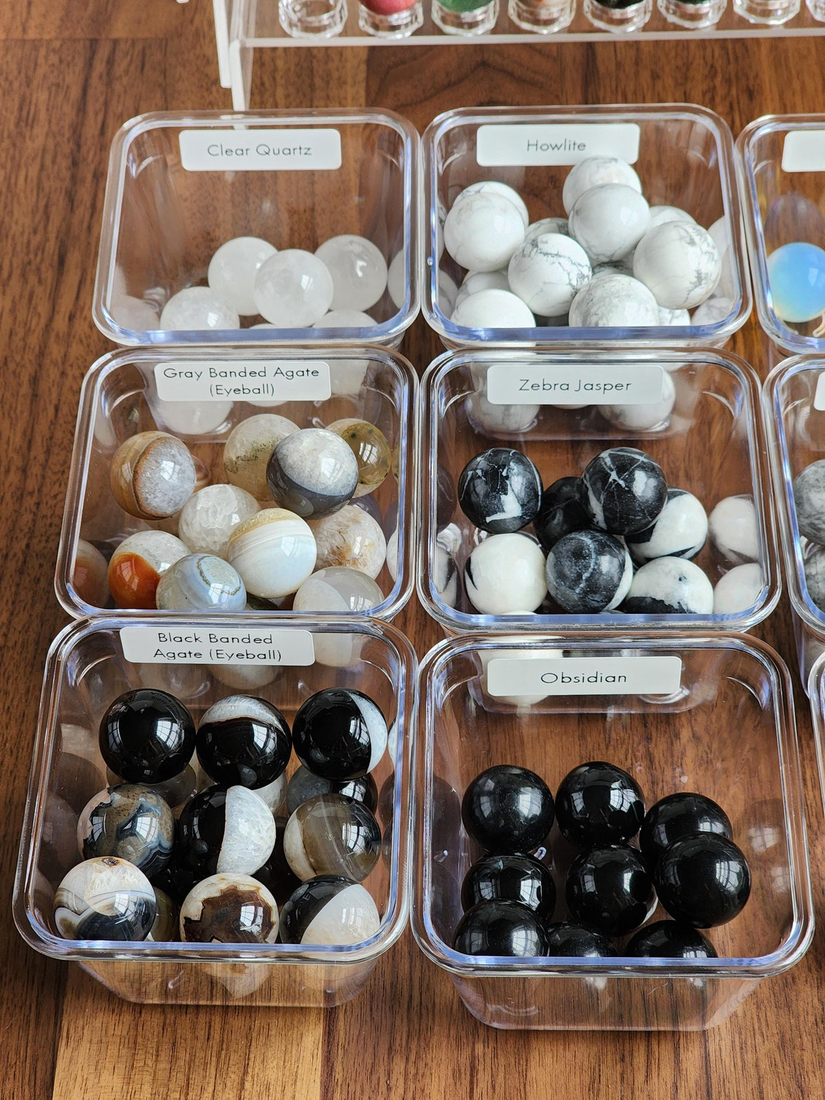 a collection of various minerals and gemstones, each in a clear plastic container, arranged on a wooden surface.