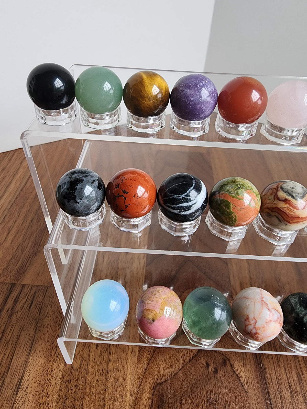 A display of various colorful gemstones and minerals arranged on a clear glass shelf.