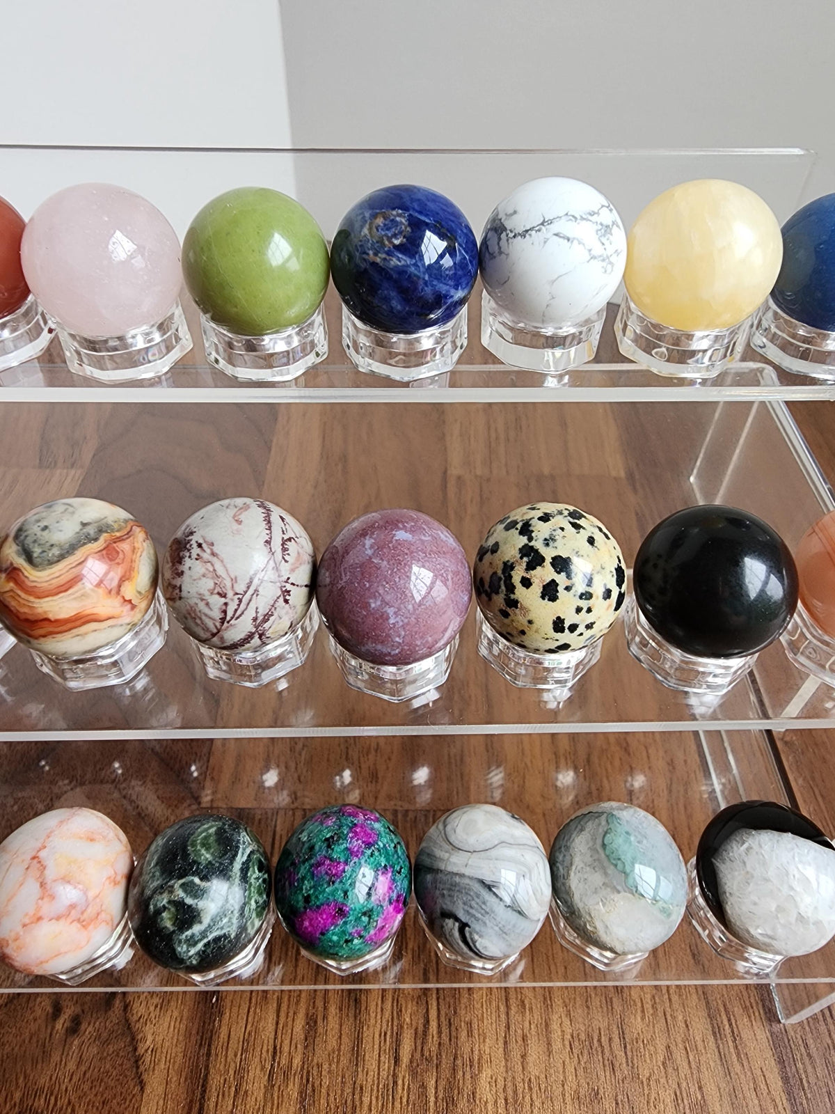 A display of various colorful gemstones and minerals arranged on a clear glass shelf.
