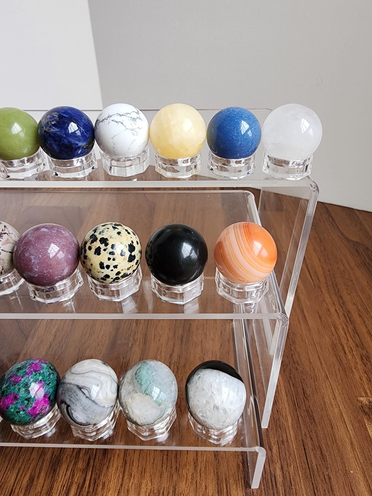 A clear glass display case containing various colorful gemstones, including amethyst, jade, and turquoise, arranged on three shelves.