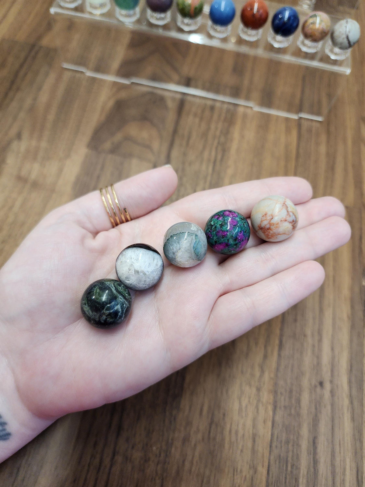 A hand holding a collection of colorful gemstones, including green, purple, and orange stones, against a wooden background.