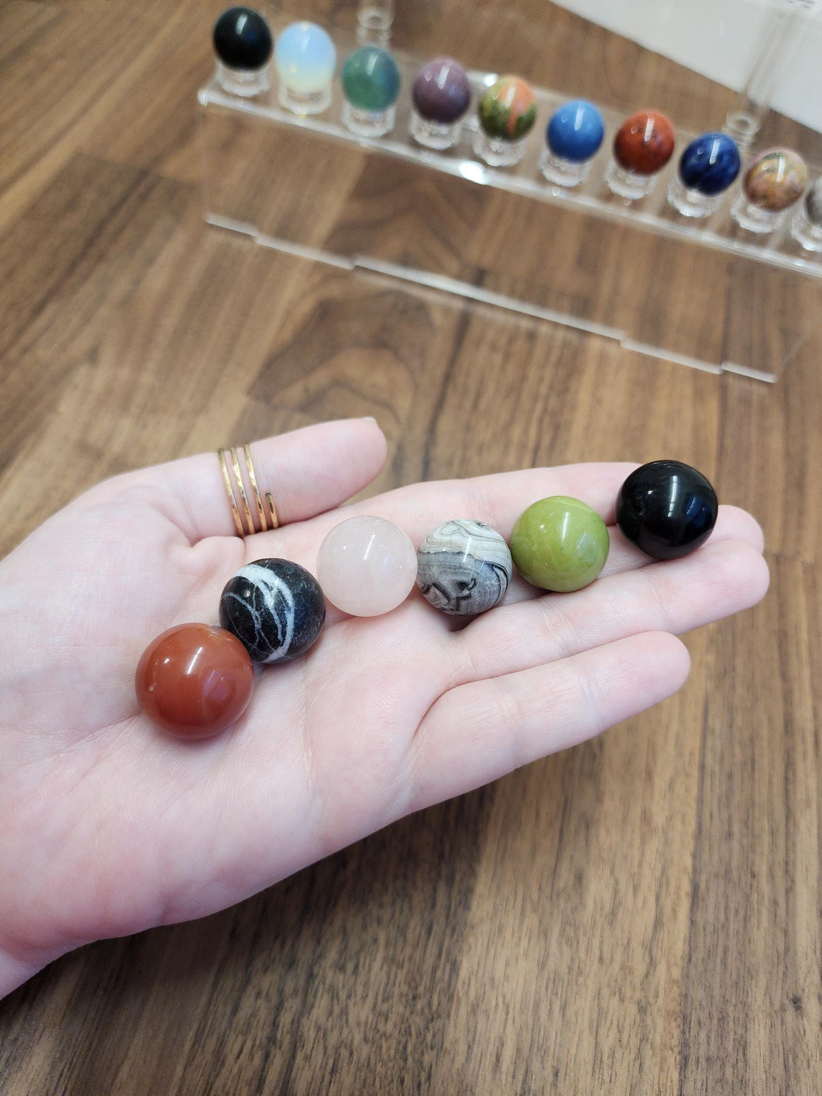A hand holding a collection of colorful gemstones, including amethyst, jade, and turquoise, against a blurred background of more gemstones.