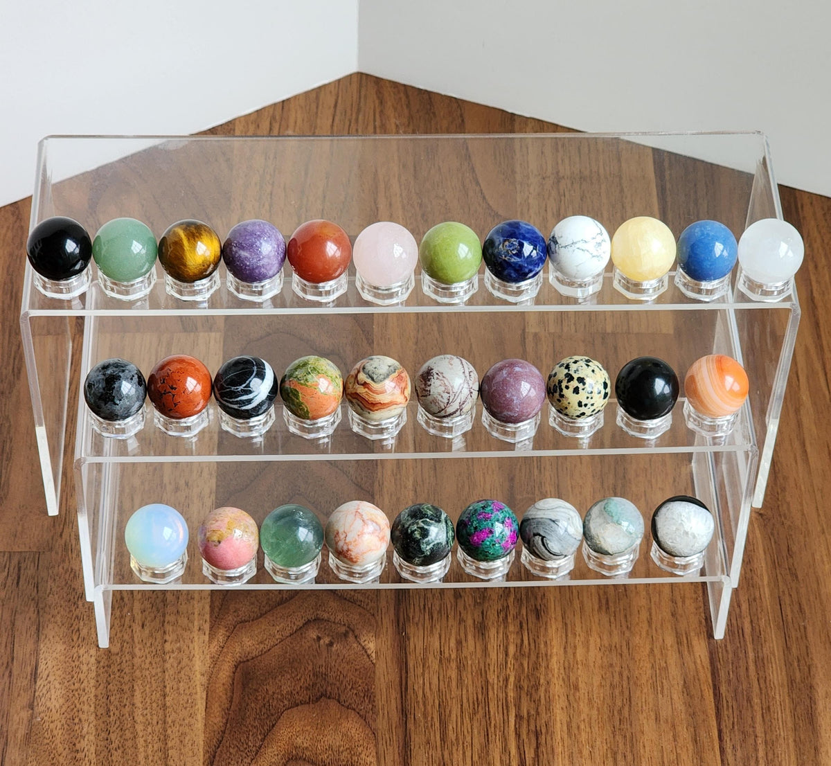 A clear glass display case containing a collection of colorful, marbled glass balls arranged on three shelves.