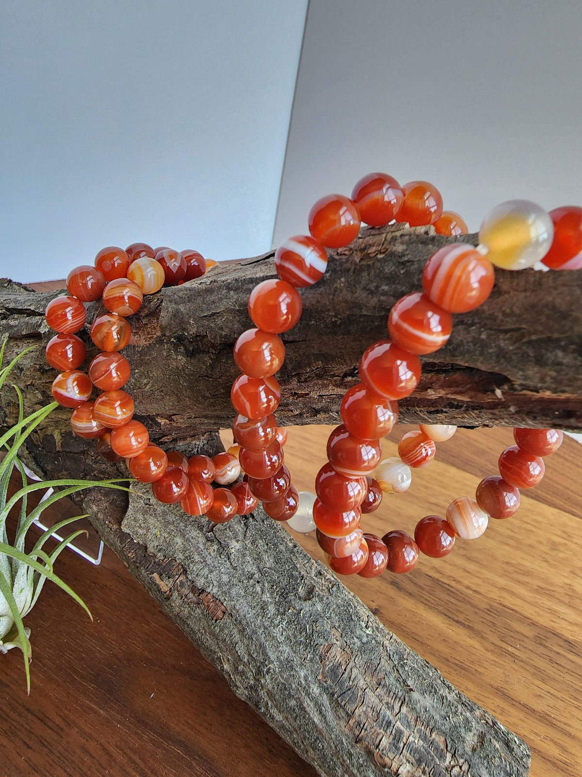 a collection of vibrant, natural-looking beads arranged on a wooden surface. The beads are in various shades of orange and red, creating a visually striking and colorful display.