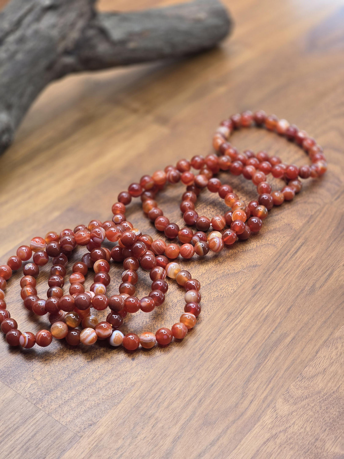 A collection of red and orange beaded bracelets arranged on a wooden surface.