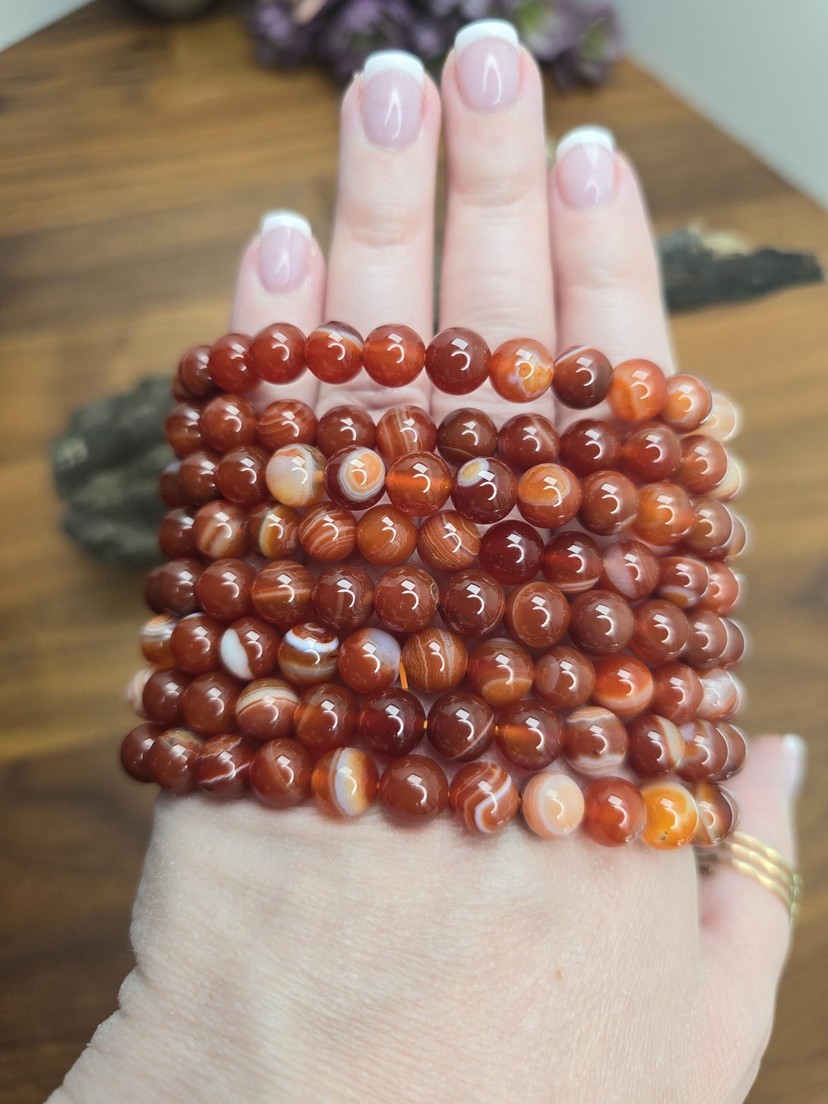 A hand wearing multiple beaded bracelets made of small, round, orange-red stones.