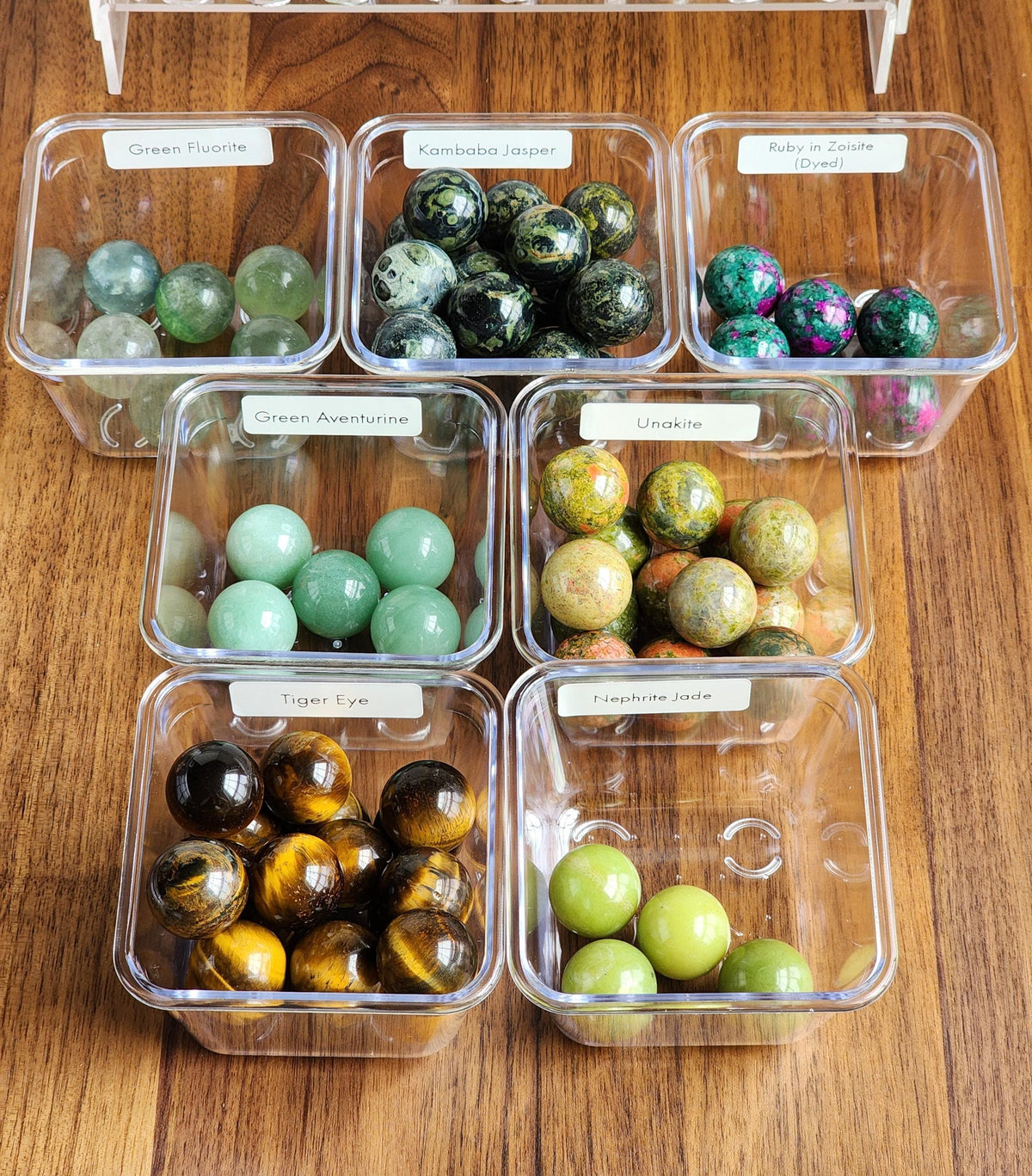 a collection of various gemstones and minerals, each in a clear plastic container, arranged on a wooden surface.