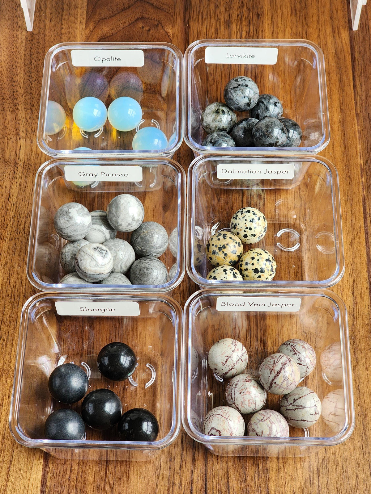 six transparent containers filled with various gemstones and stones, each labeled with a different name.