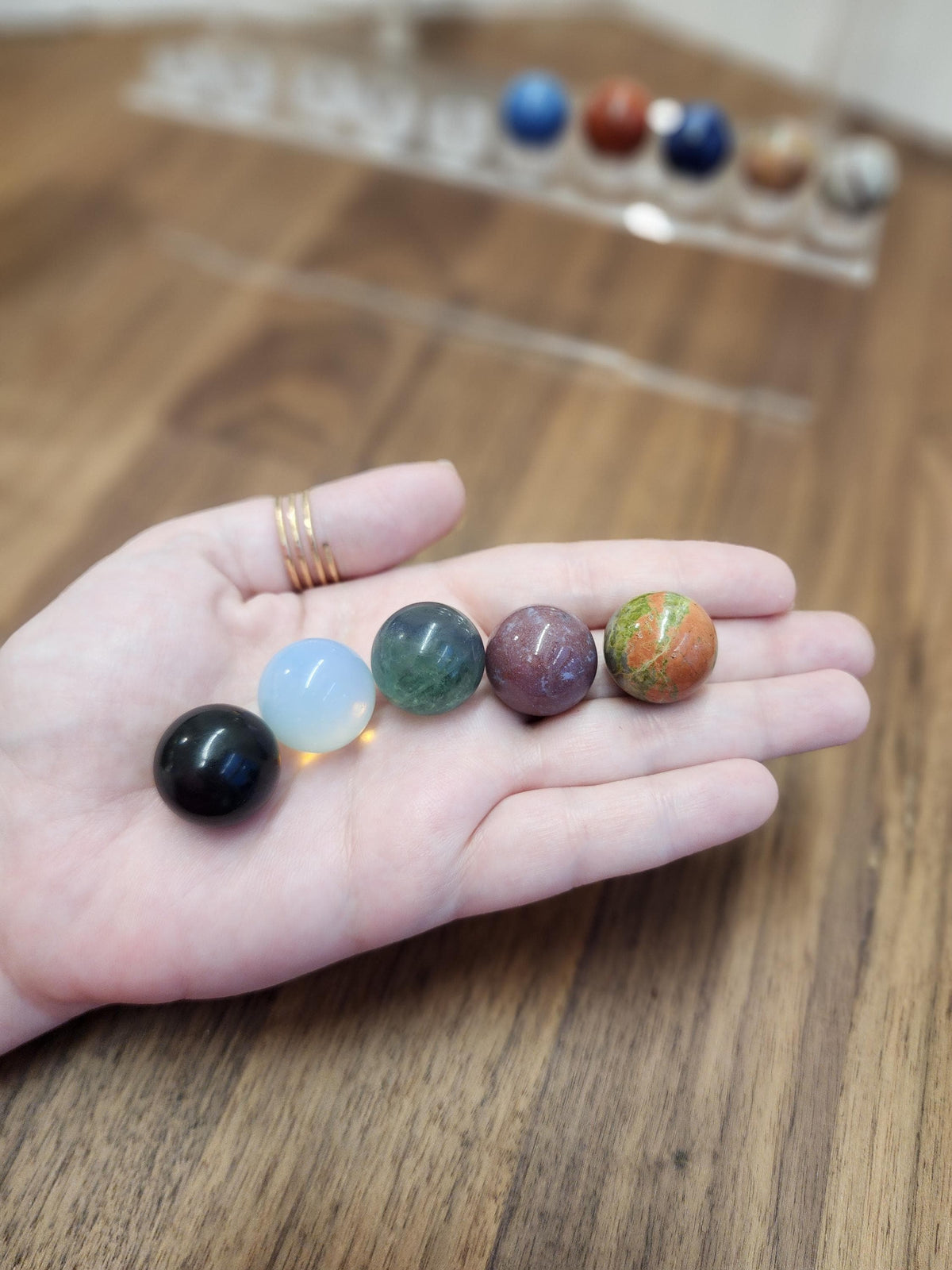 A hand holding a collection of colorful gemstones, including blue, green, purple, orange, and brown stones, against a blurred background.