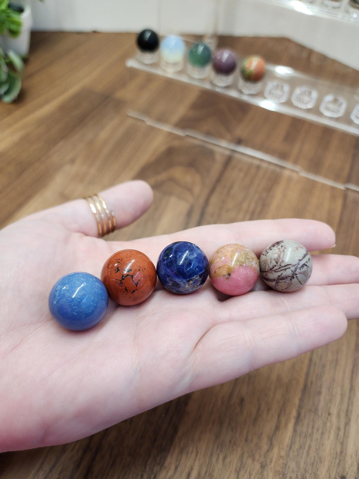 A hand holding five colorful gemstones, including blue, orange, pink, and brown stones, arranged in a row.