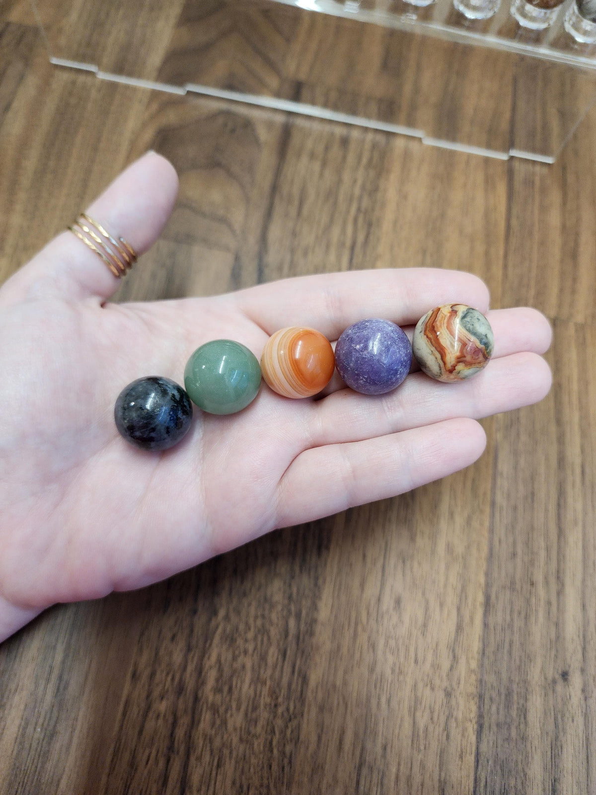 A hand holding five colorful gemstones, including a green stone, an orange stone, a purple stone, a brown stone, and a black stone.