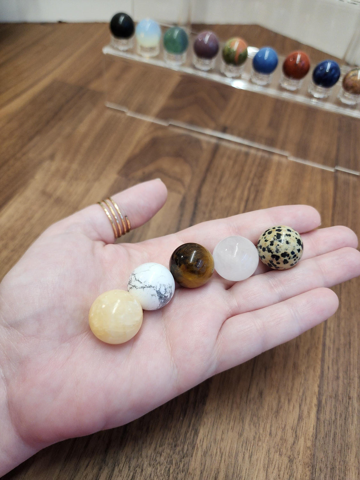 A hand holding a collection of colorful gemstones, including amethyst, jade, and turquoise, against a wooden background.