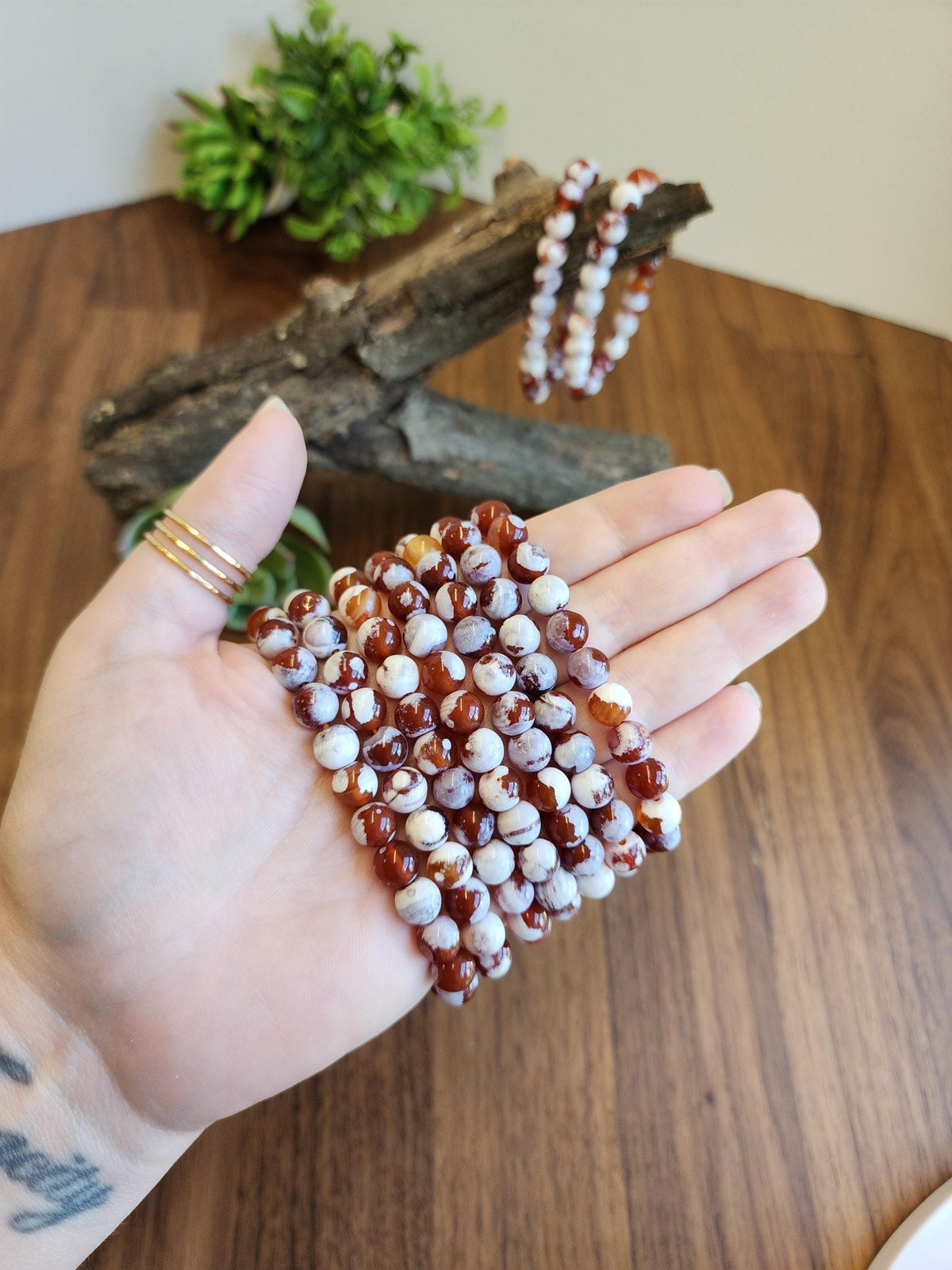 A hand holding a collection of colorful beaded bracelets against a wooden background.