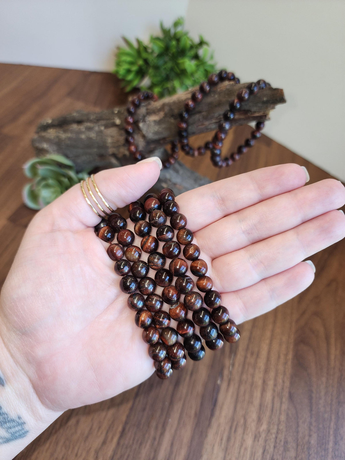 A hand holding a bunch of brown beads, possibly beaded or made of wood, with a plant in the background.