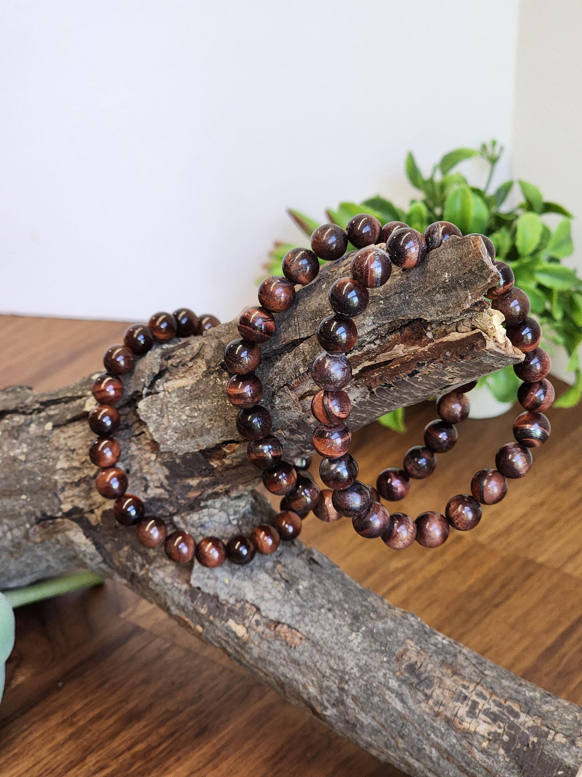 a pair of brown wooden beaded bracelets resting on a wooden surface, with a potted plant visible in the background.