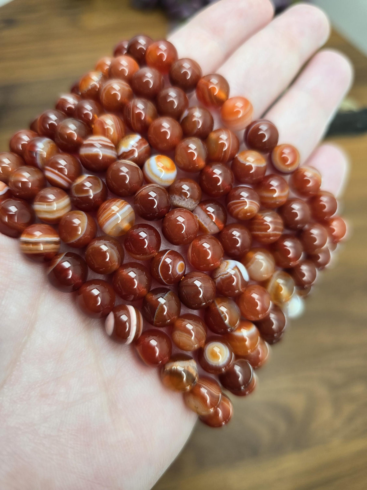 A hand holding a collection of small, round, orange-colored stones or beads.