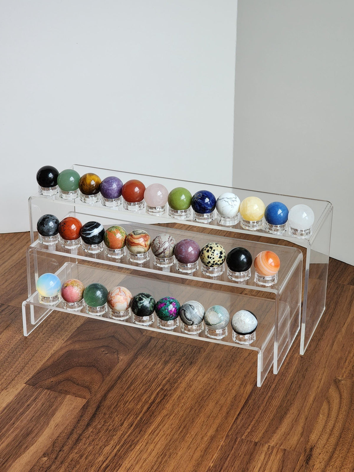 A clear glass display case containing various colorful gemstones, including clear gemstones and gemstone-like objects, arranged on multiple shelves.