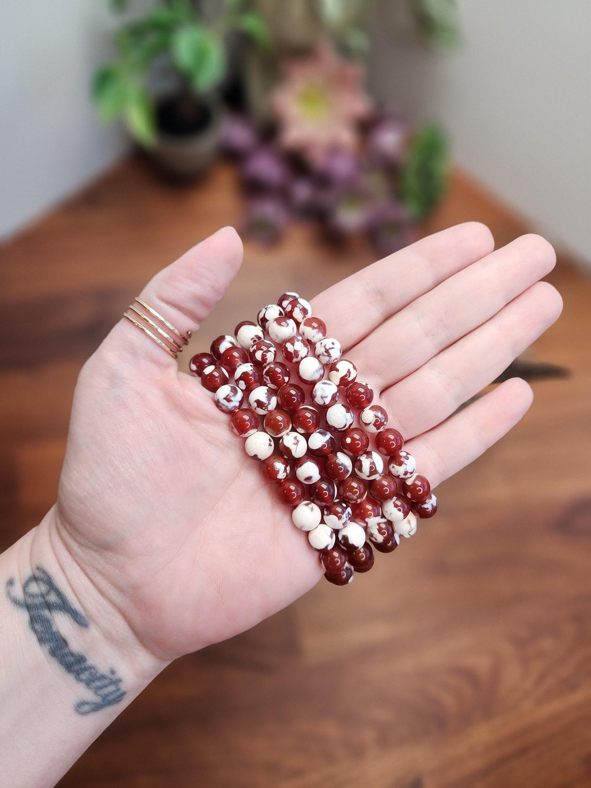 A hand holding a cluster of red and white beads against a blurred background with flowers.