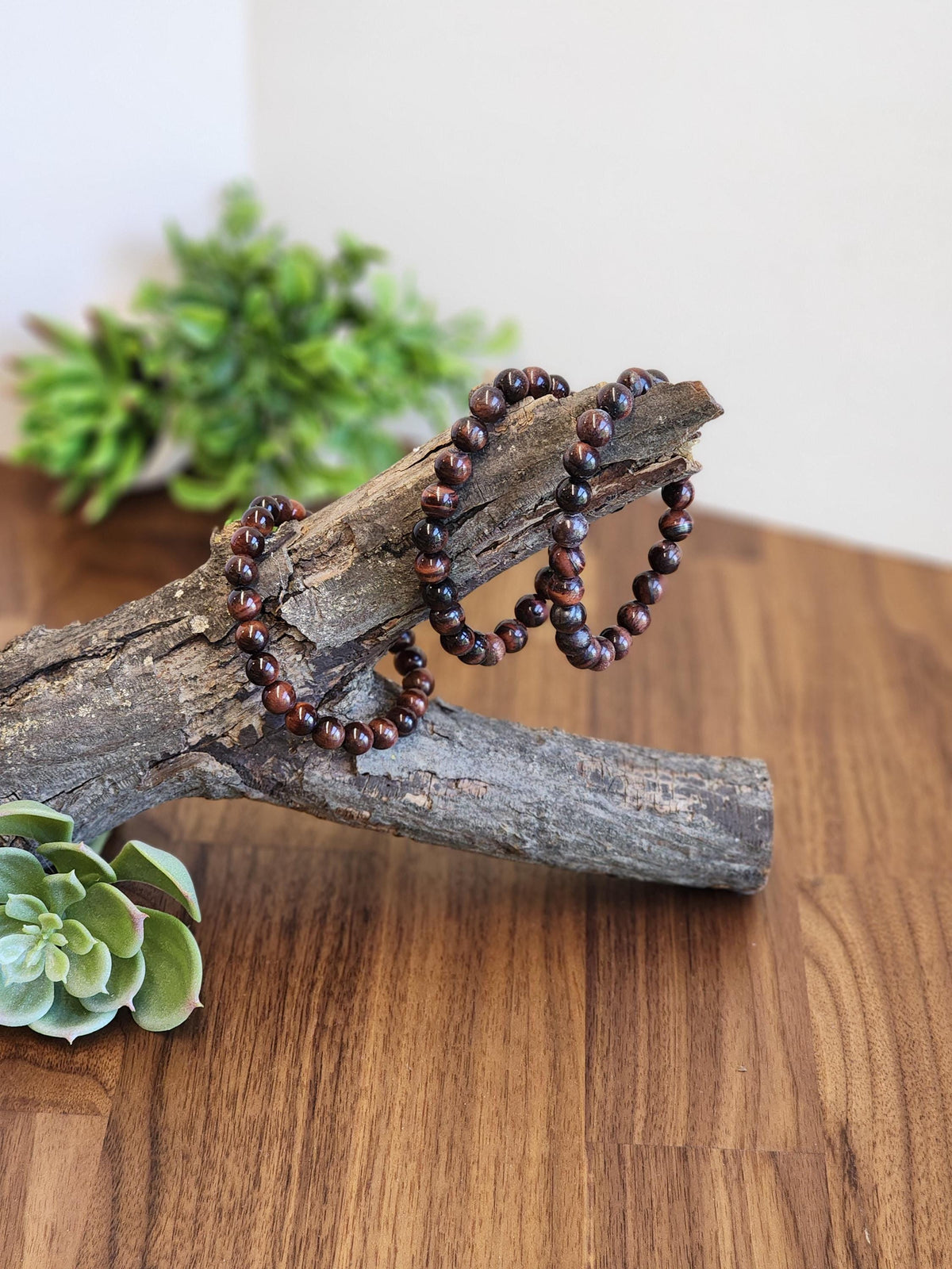 a pair of brown beaded bracelets resting on a wooden surface, with a green plant in the background.