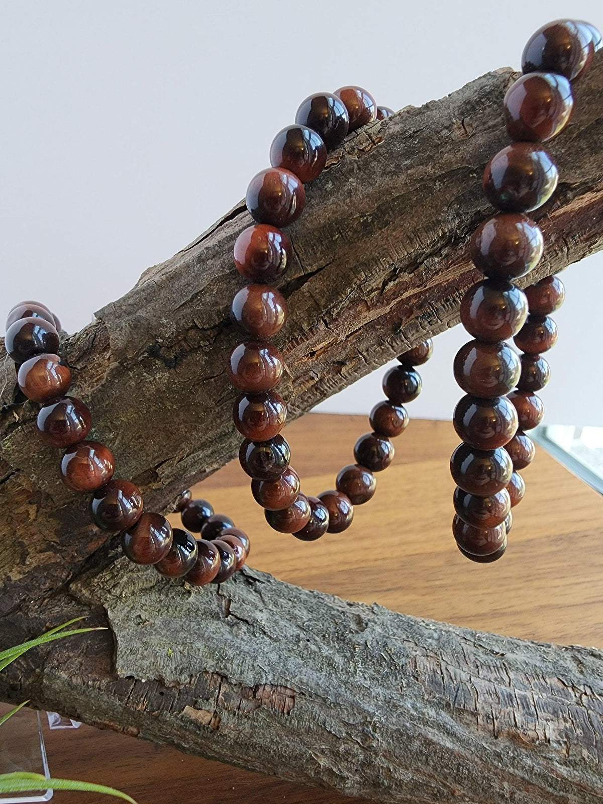 A necklace of brown wooden beads is hanging from a wooden branch.