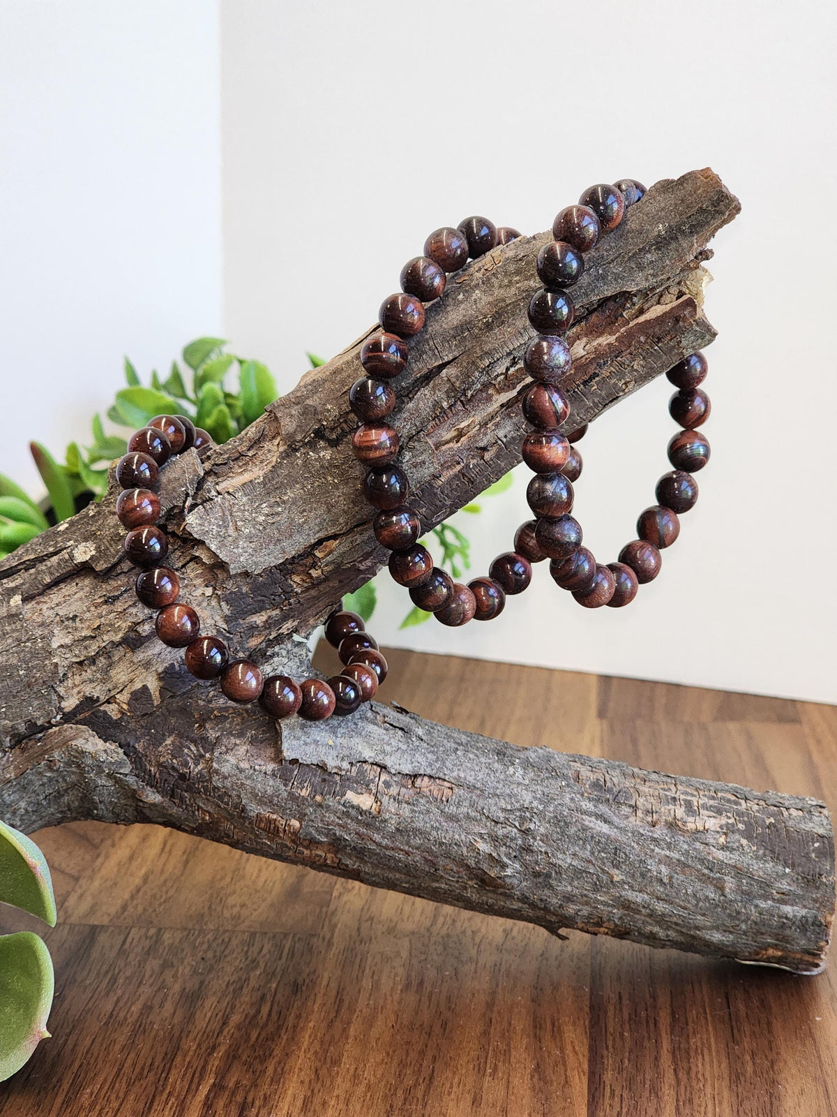a pair of brown beaded bracelets resting on a wooden surface, with a plant visible in the background.