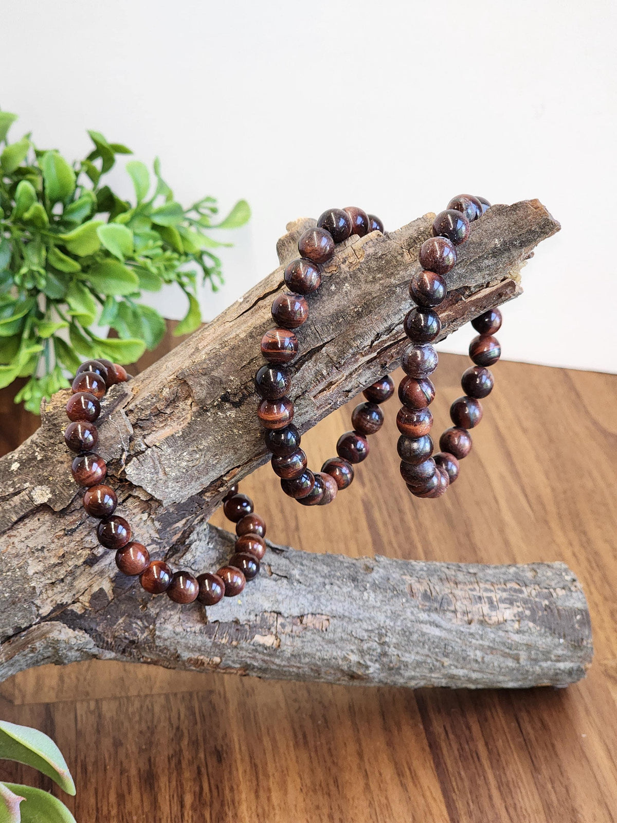 a pair of brown beaded bracelets resting on a wooden surface, with a plant in the background.