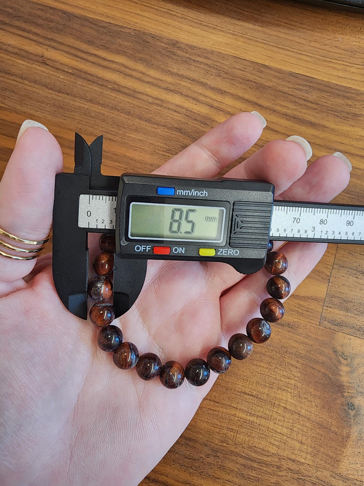 A person's hand holding a digital caliper and measuring a bracelet.