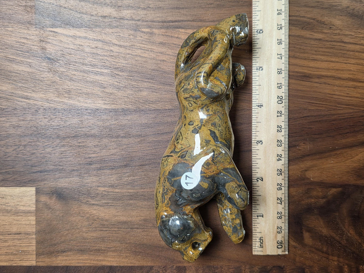 A ceramic figurine of a panther is placed next to a ruler on a wooden surface.