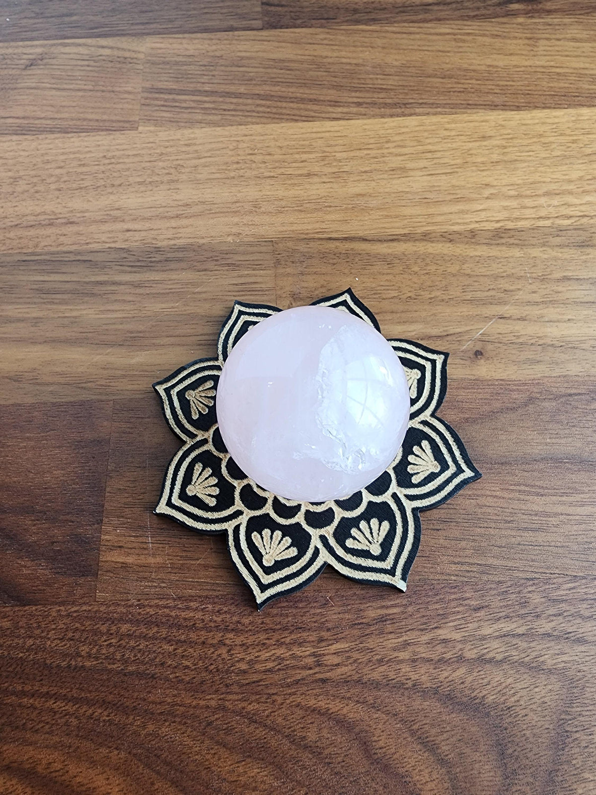 A white crystal ball rests on a black and gold decorative mat, placed on a wooden surface.