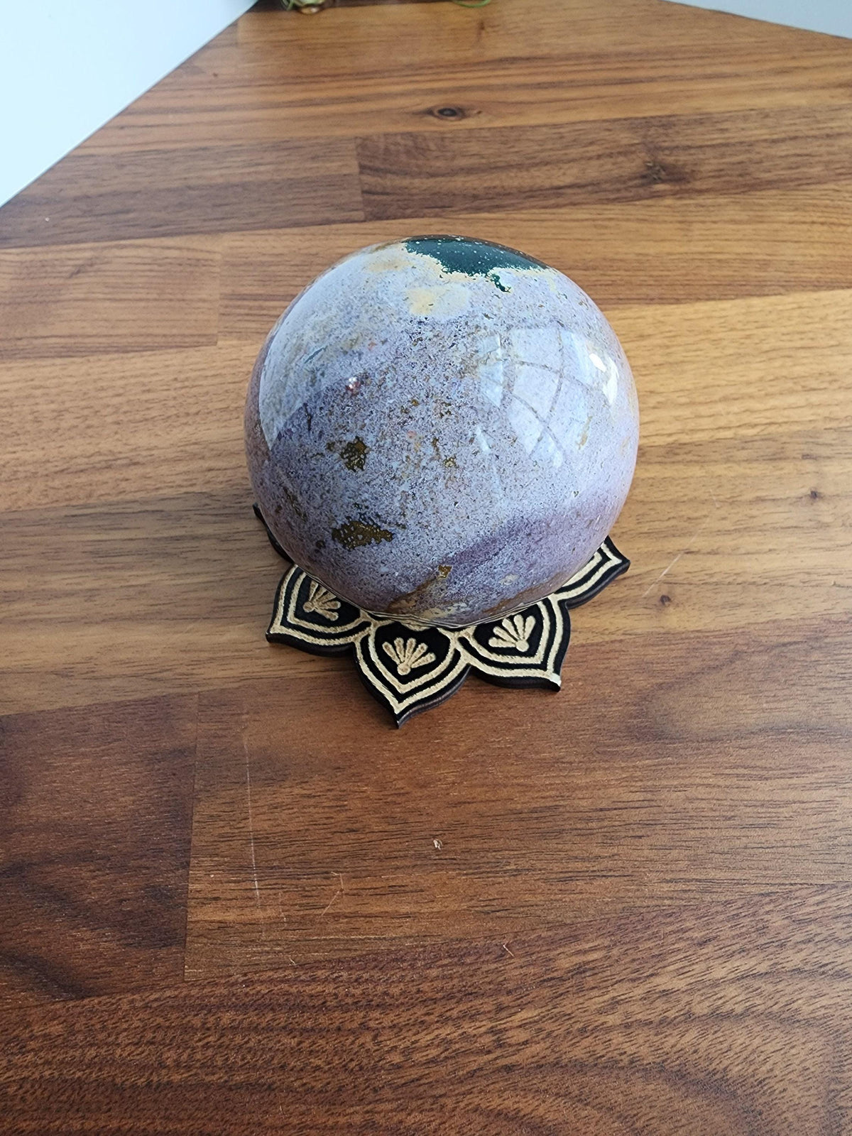 A purple and green gemstone sits on a black and gold decorative stand on a wooden surface.