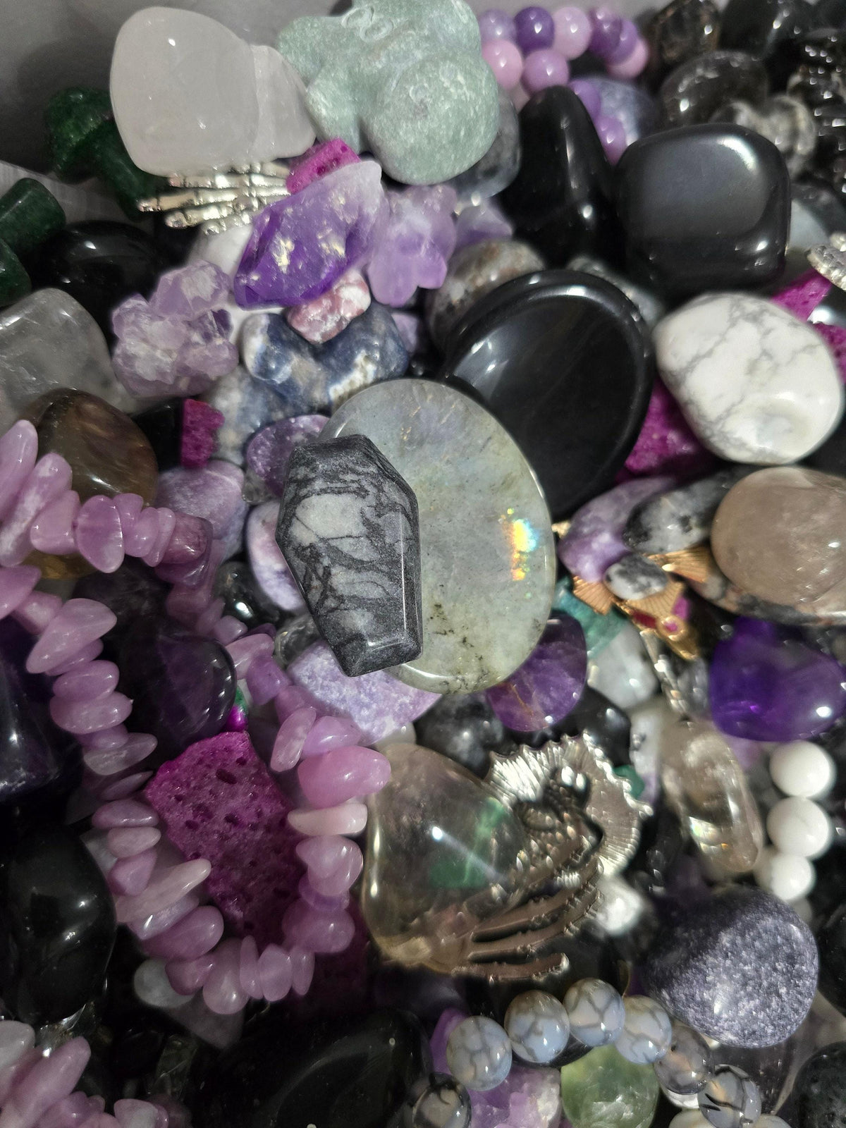 The image is a close-up of various gemstones and crystals, including amethyst, quartz, and black onyx, arranged in a visually appealing manner.