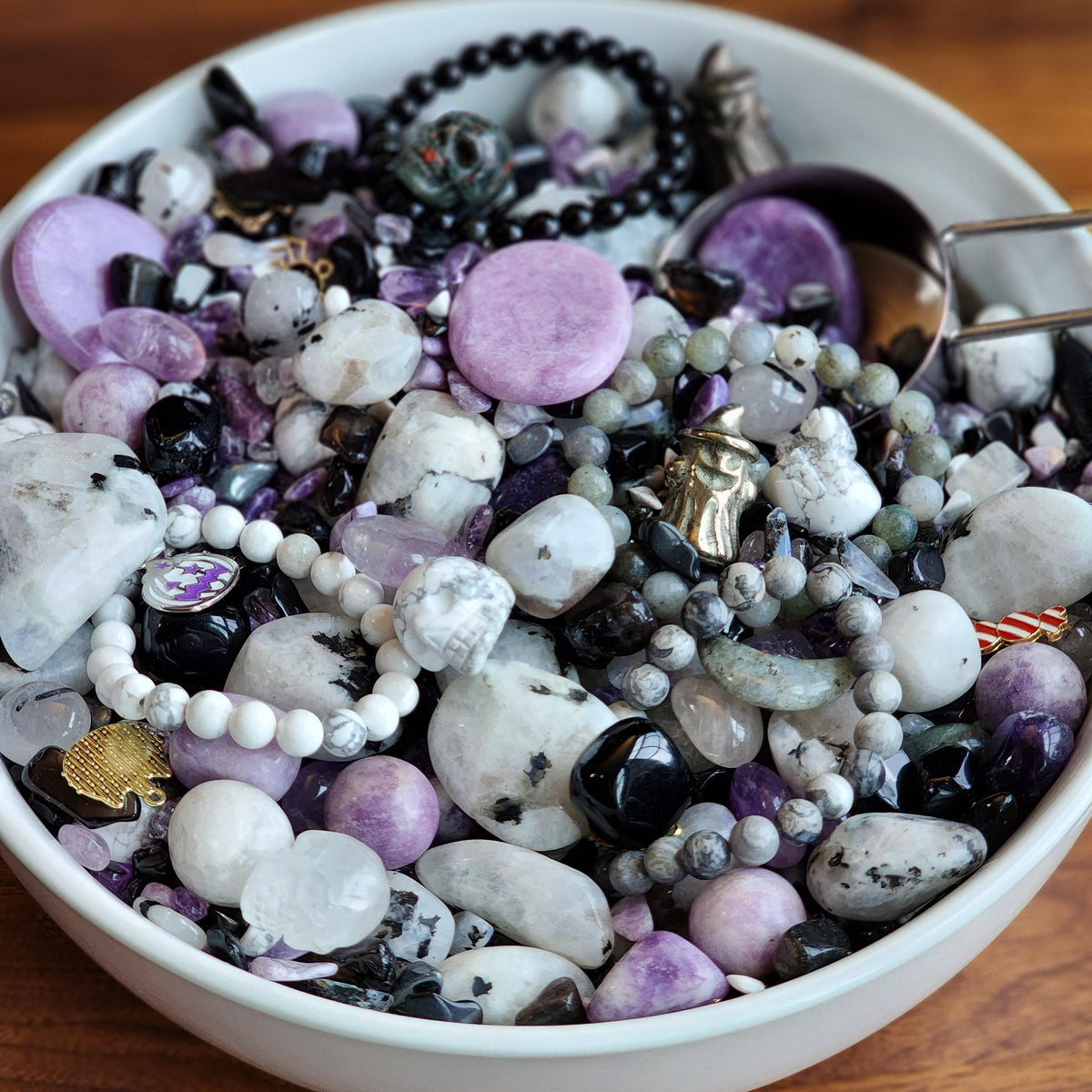 A bowl filled with various colorful and shiny stones, including purple, white, black, and gray stones, as well as some beads and other decorative items.