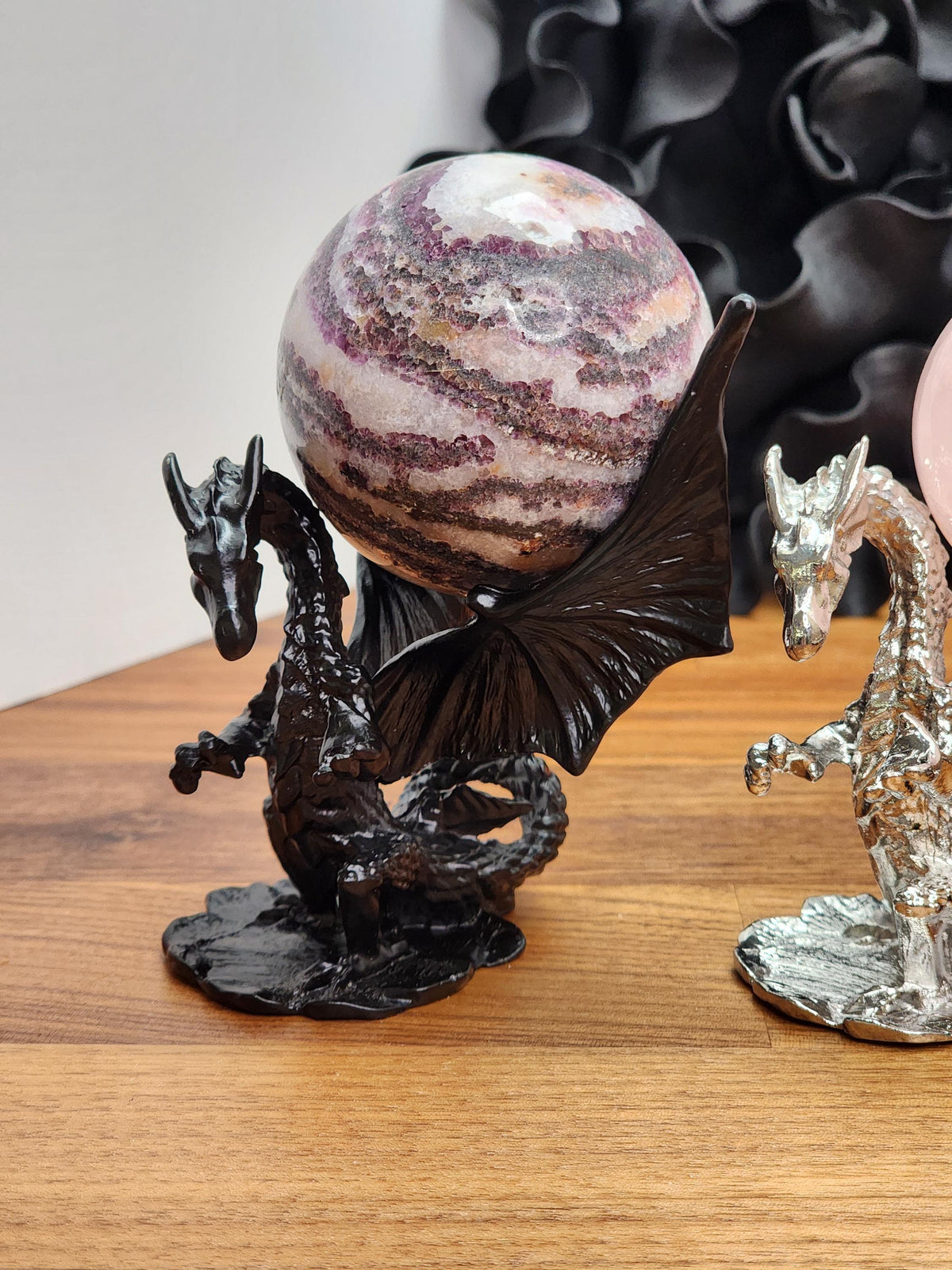 a dragon figurine holding a large, colorful ball on a wooden surface.