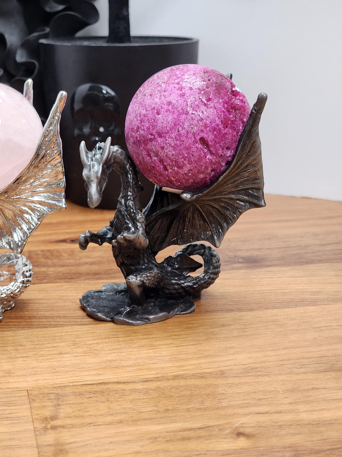 A dragon figurine holding a large, round, pink object on a wooden surface.