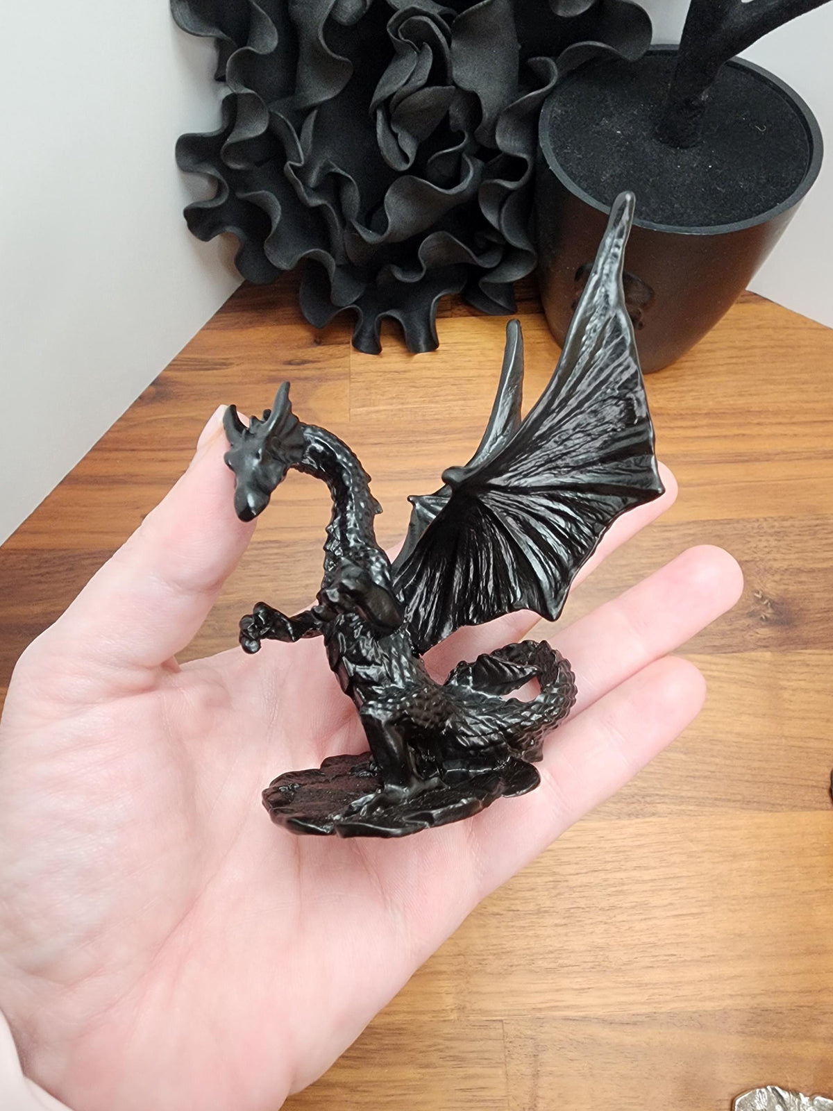 A hand holding a black dragon figurine against a wooden background.