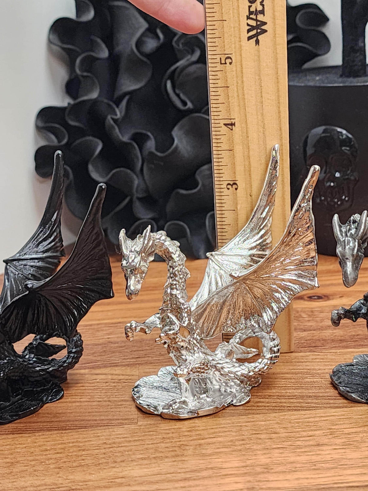 a metallic dragon figurine on a wooden surface, with a ruler placed next to it to indicate its size.