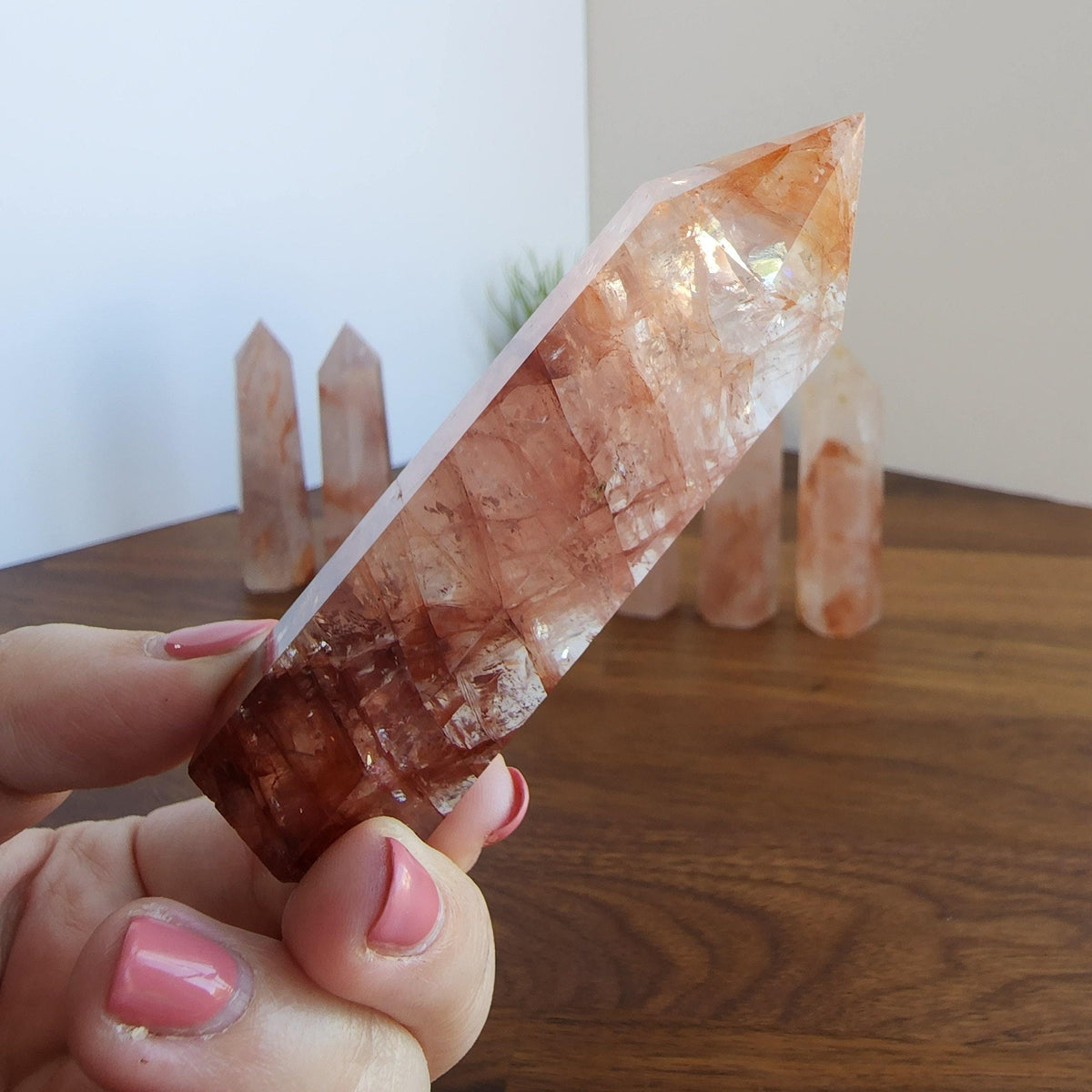 A hand holding a clear crystal with a reddish-brown hue, set against a blurred background of additional crystals.