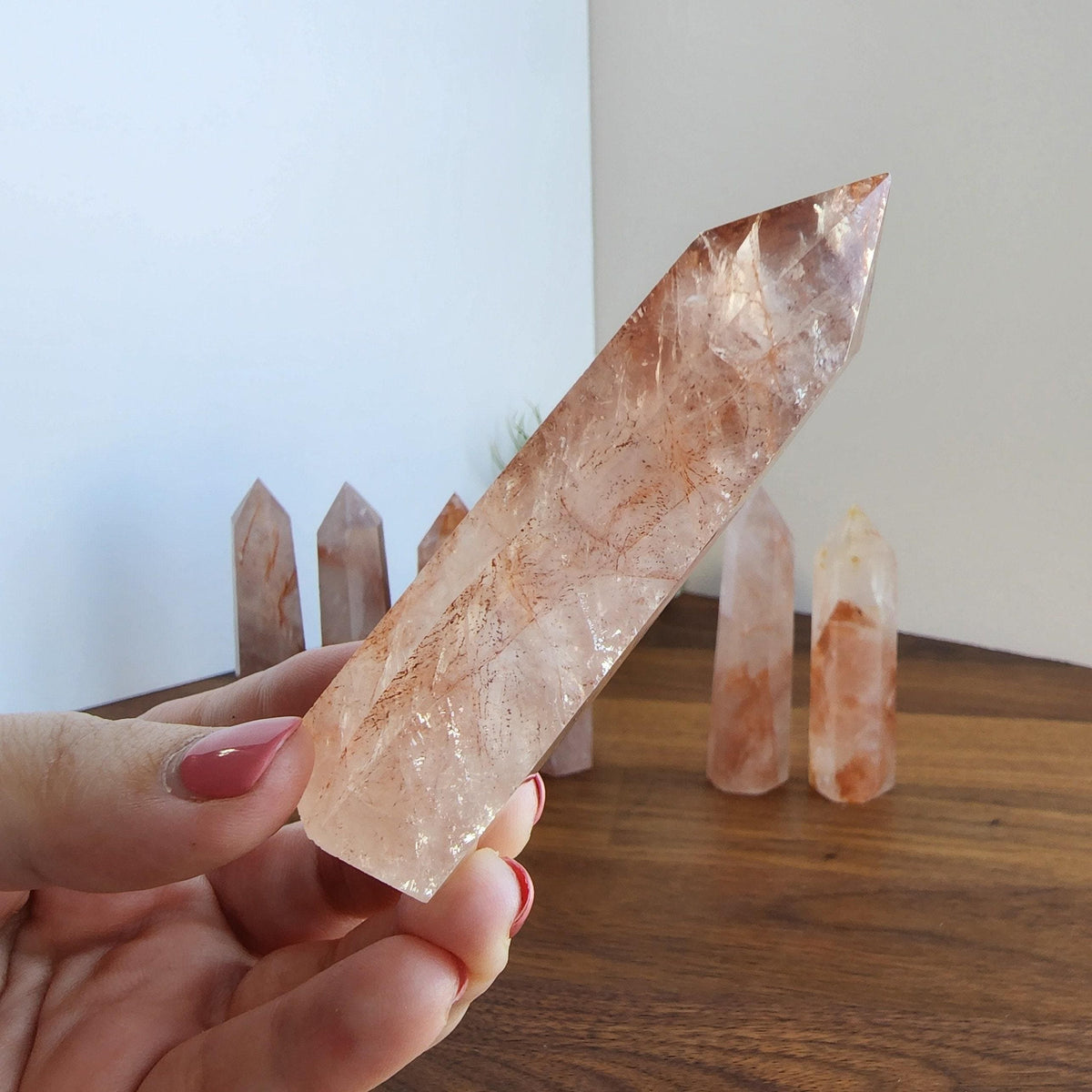 A hand holding a clear crystal with a brownish hue, surrounded by several similar crystals on a wooden surface.