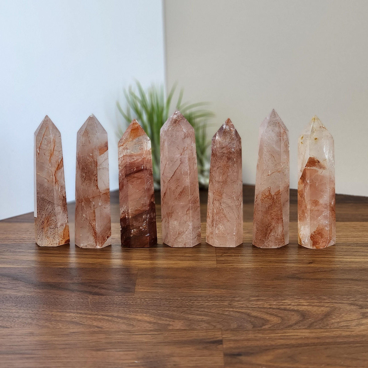 A row of seven clear quartz crystals with varying colors, arranged on a wooden surface.