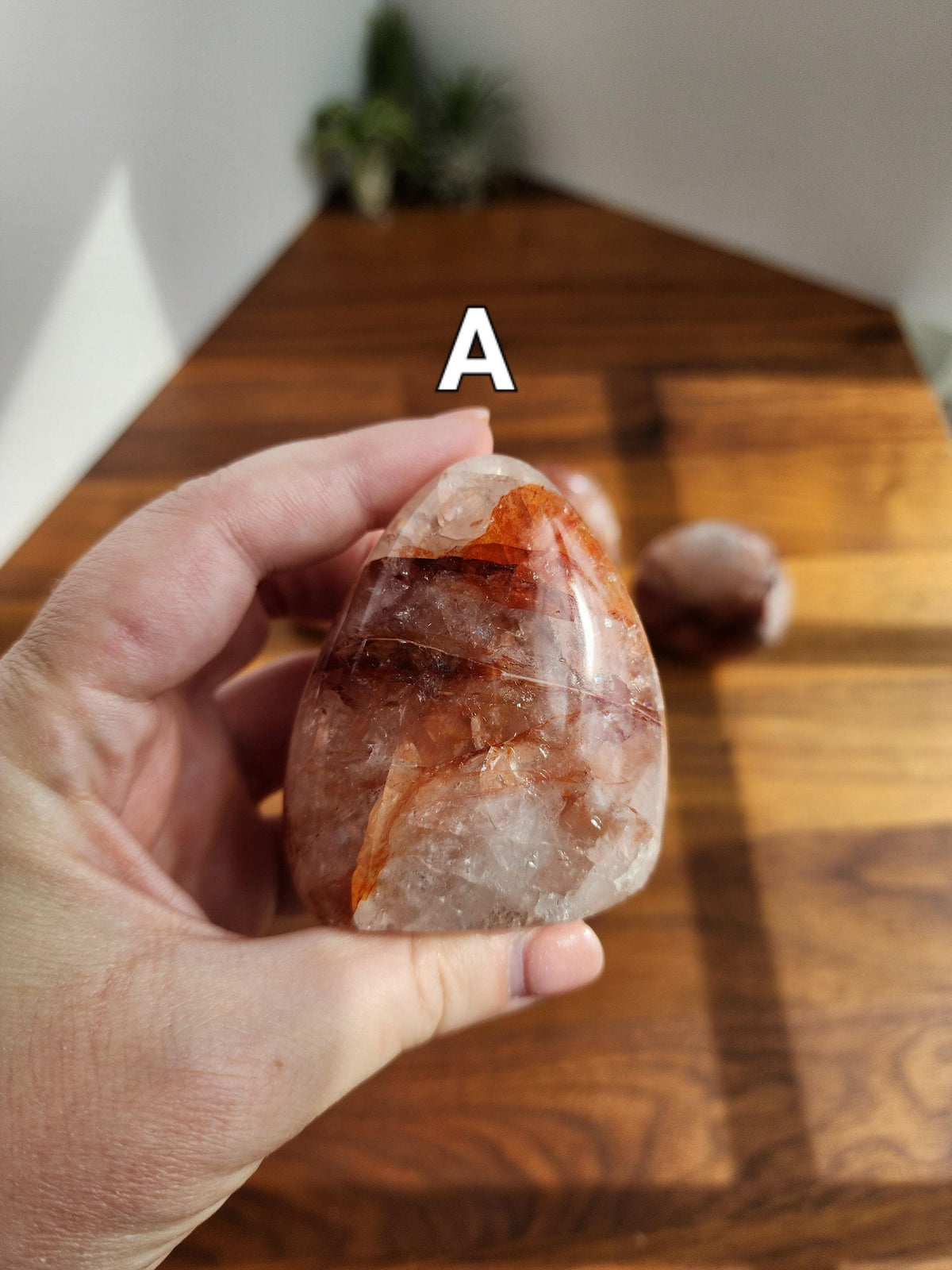 A hand holding a clear, oval-shaped stone with a reddish-brown hue, set against a wooden background.