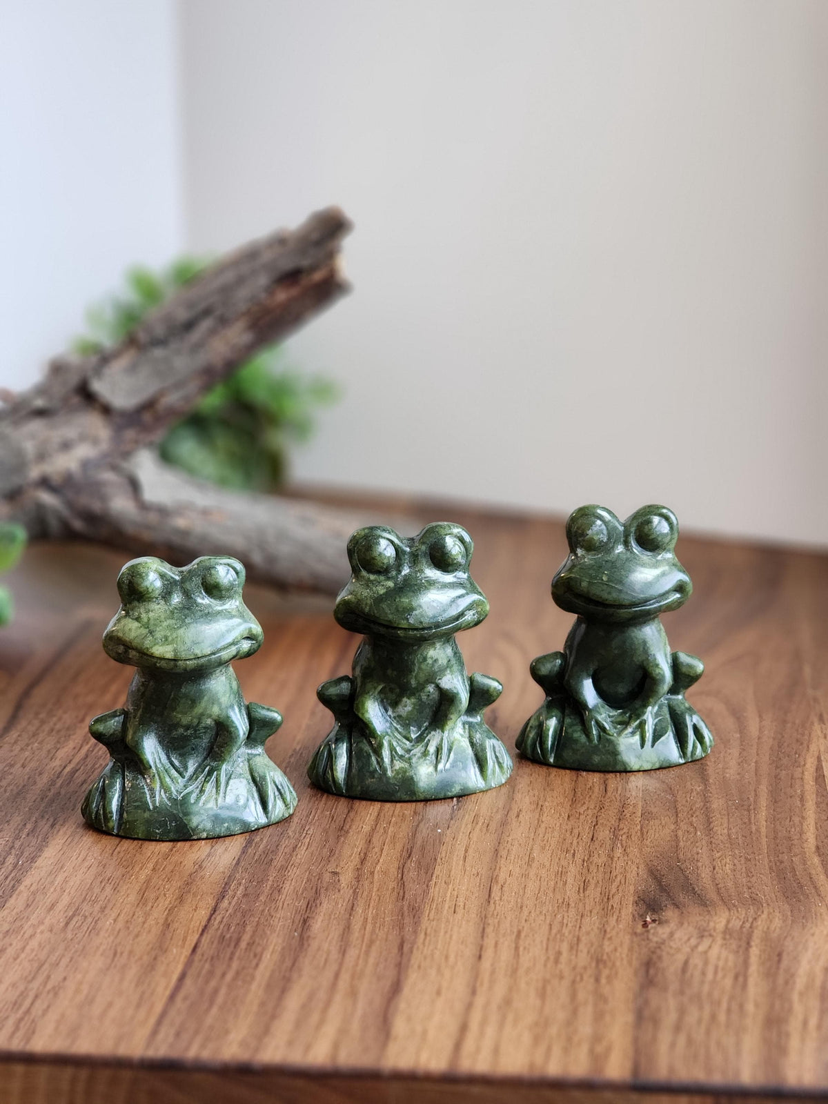 May include: Three small, green frog figurines carved from stone. Each frog is seated with its legs tucked and has large, round eyes. The figurines are displayed on a wooden surface.