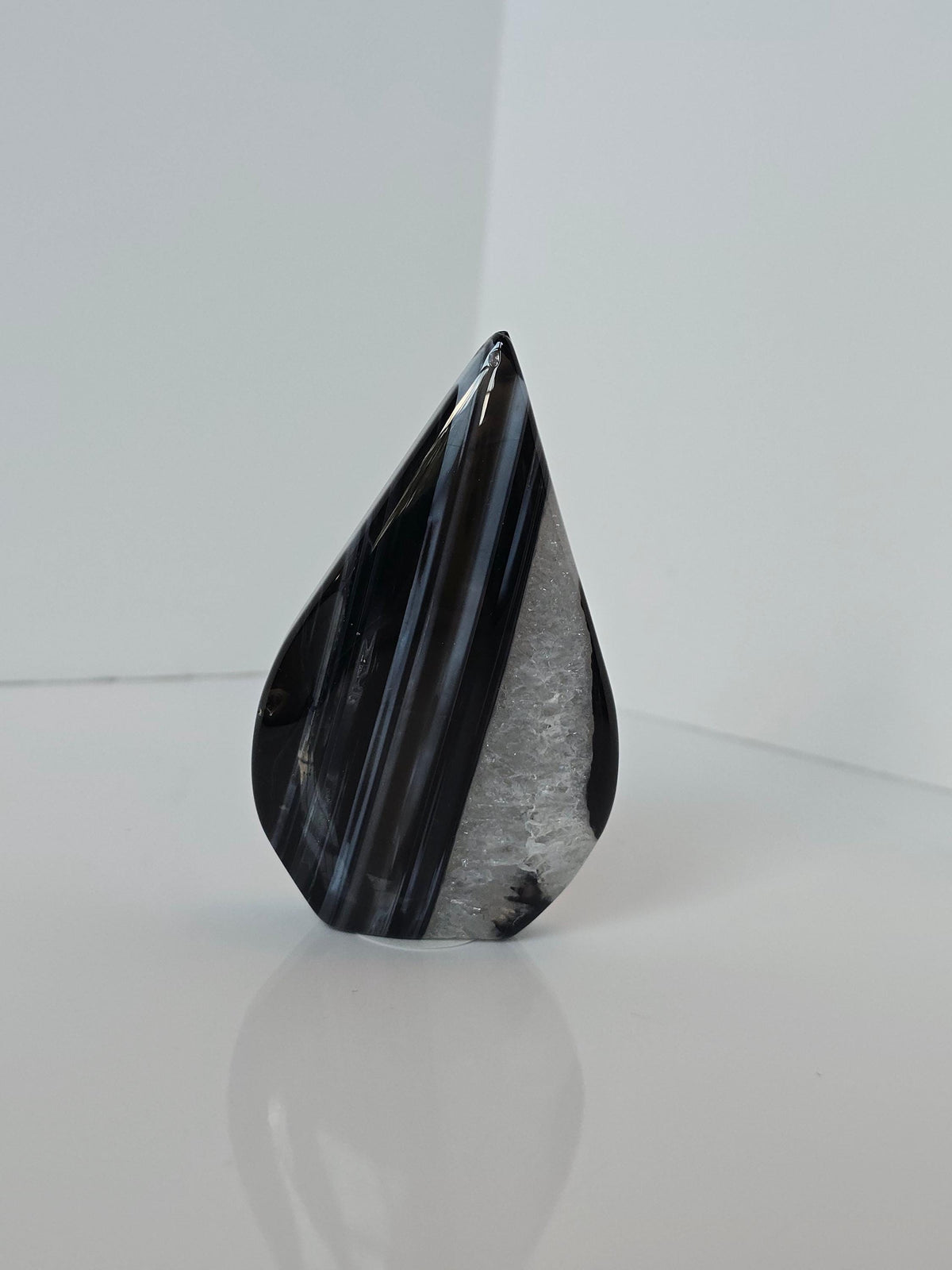 A black and white speckled rock sits on a white surface, its surface reflecting the light.