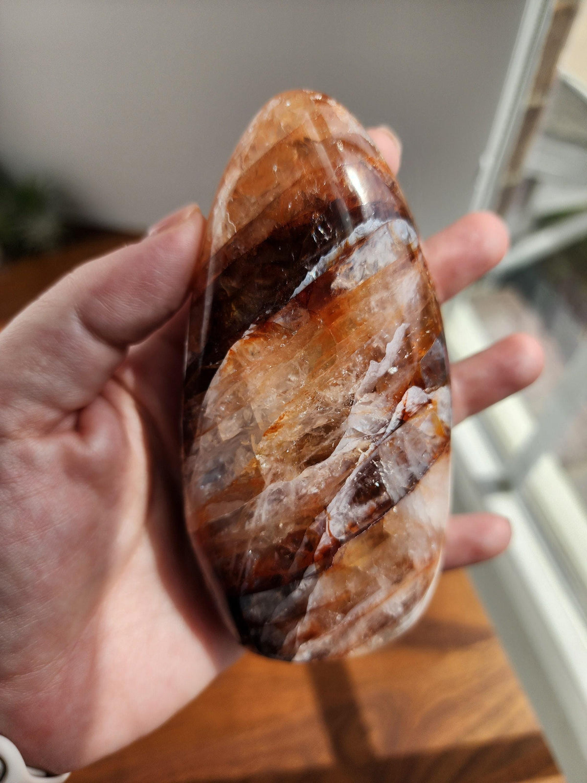 A hand holding a large, multicolored rock or gemstone, with a blurred background that appears to be a window or a similar indoor setting.