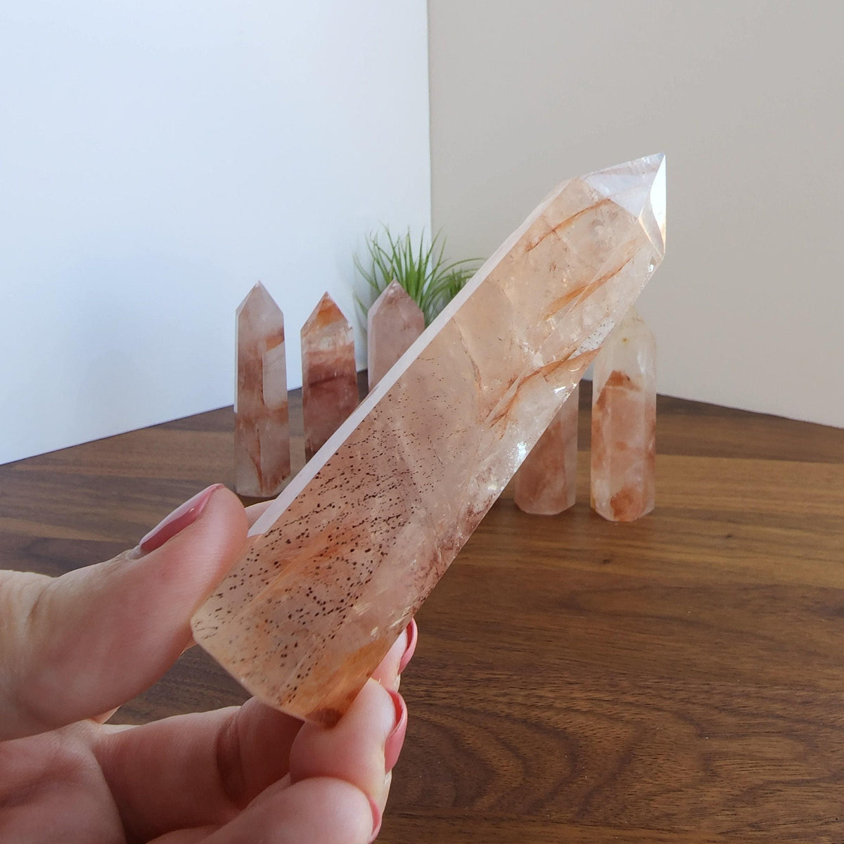 A hand holding a clear crystal with a speckled surface, surrounded by several similar crystals on a wooden surface.