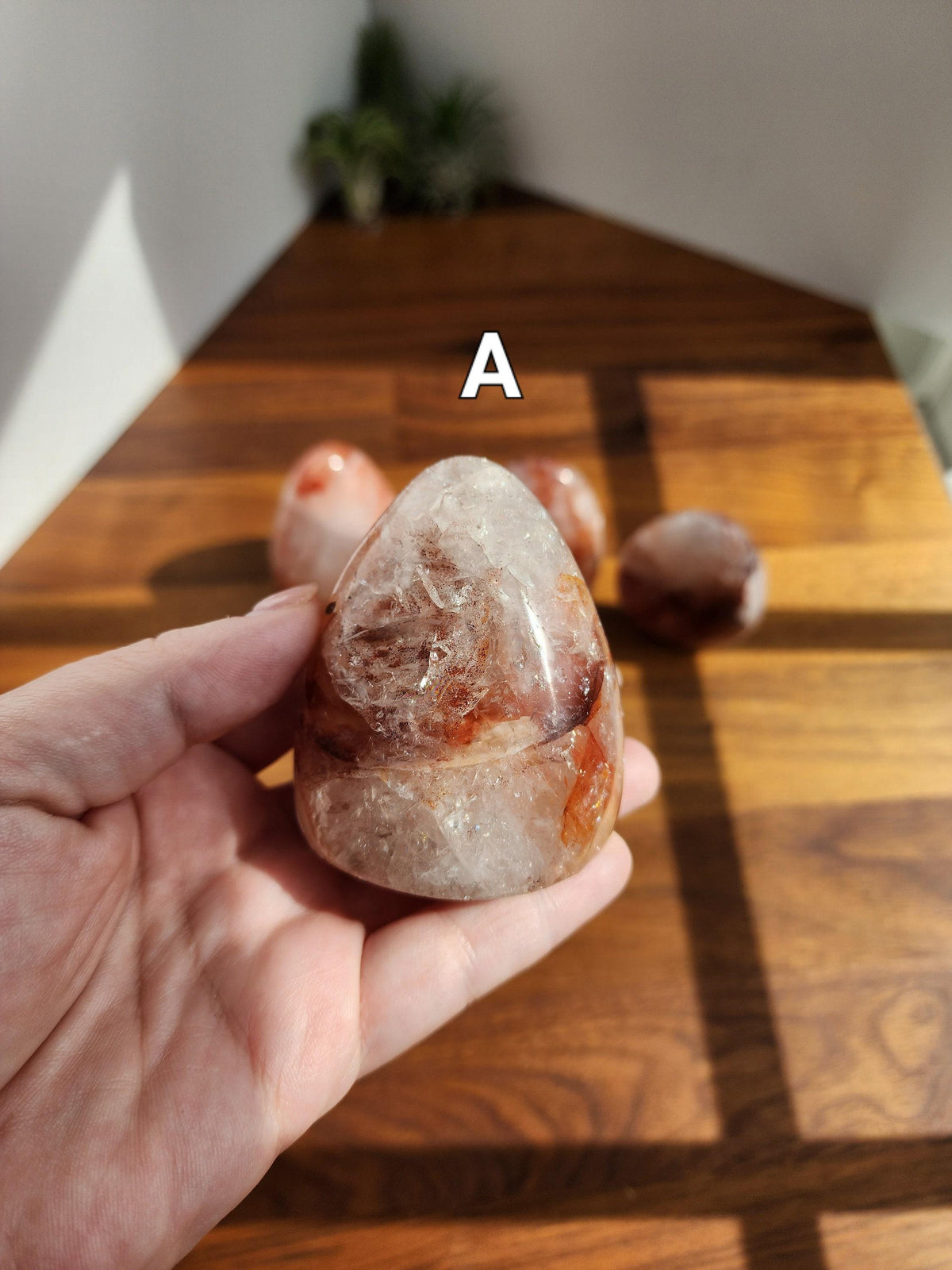 A hand holding a clear crystal with a red and white pattern, against a wooden background.